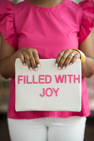 model holding white canvas pouch with hot pink beaded block letters saying "filled with joy"
