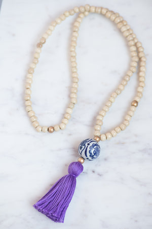wooden beaded necklace with gold beaded accents and porcelain chinoiserie bead, and purple tassel.