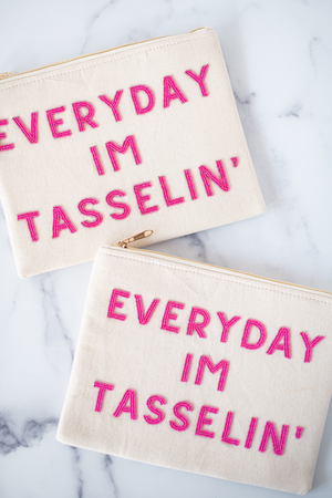 two white canvas pouches with hot pink beaded accents with the words "everyday I'm tasseling" in block letters on marble background