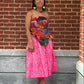 Woman in a colorful strapless top and pink skirt standing against a brick wall.