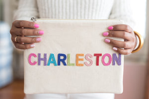 model holding charleston canvas pouch with beaded block lettering spelling out Charleston in hot pink, purple, teal, blue, lime green, orange, light pink, and red beading