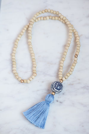 Wooden beaded necklace with golden bead accents, porcelain chinoiserie bead, and cornflower blue tassel